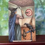 Two of Swords - A young witch throwing knives at a dart board, a cat and a raven as her companions.